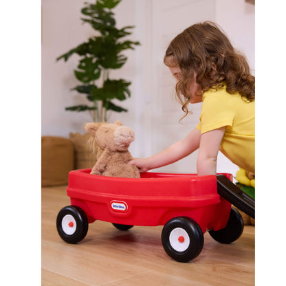 Child playing with a red toy wagon containing a teddy bear in a home setting.