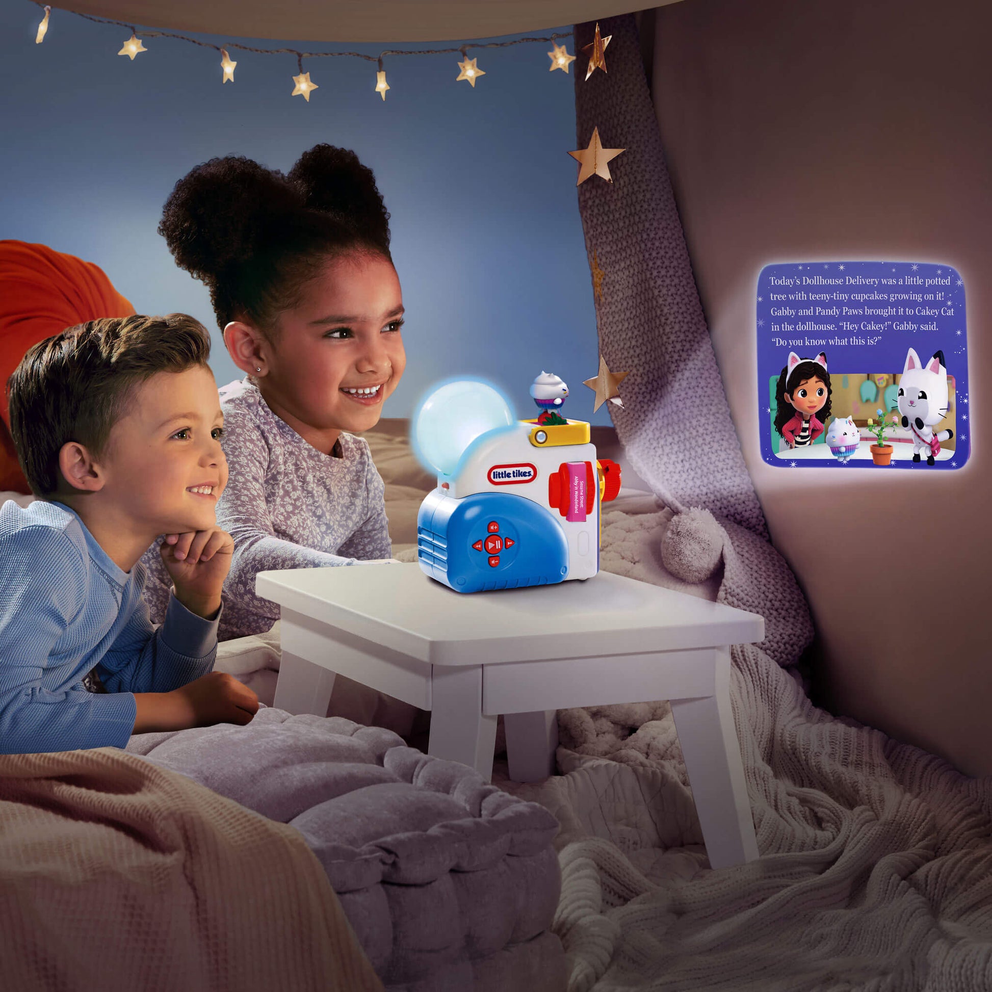 Two children sitting in a cozy bed-like room, looking at a small toy projector on a white table that casts a glowing light and story text onto a wall.