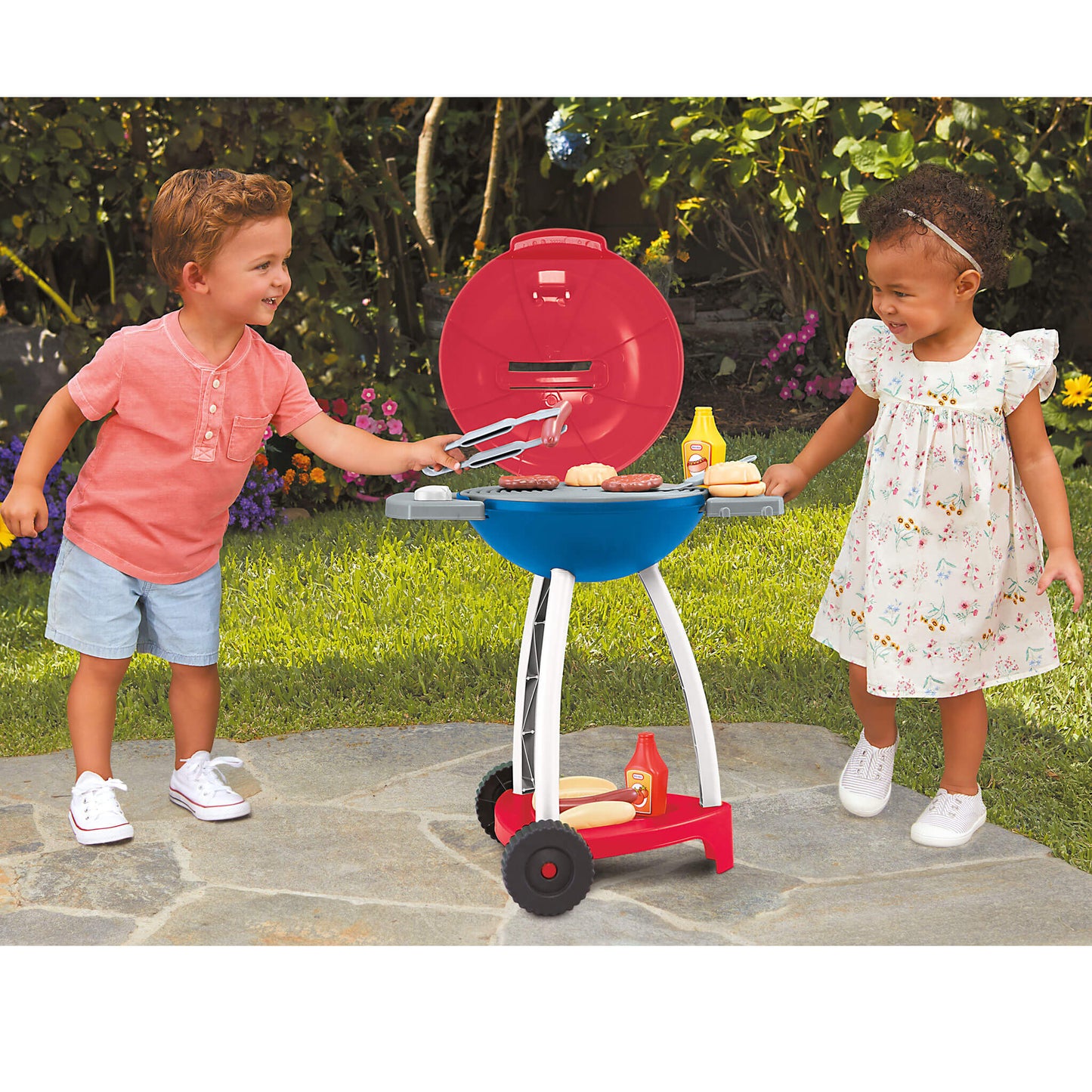 Two children playing with a toy barbecue set outdoors.