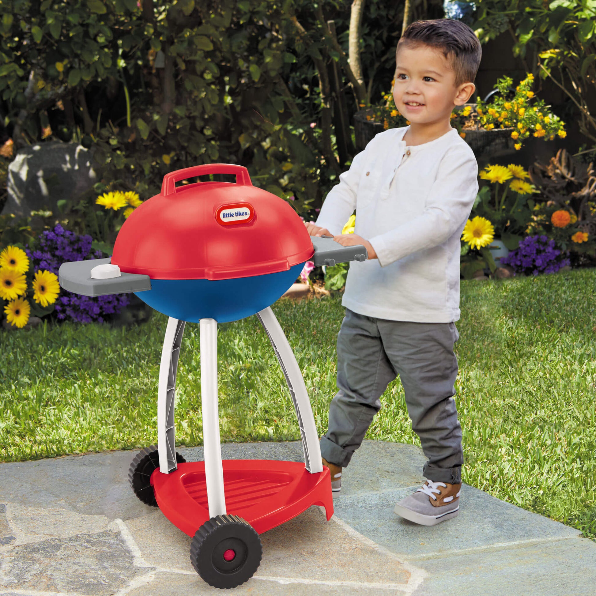Child moving toy barbecue set, with wheels, outdoors on a patio