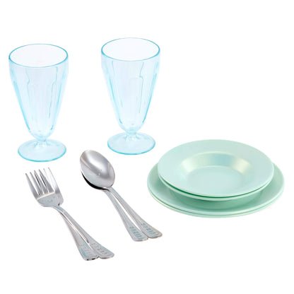 A children's tableware set featuring two light blue goblets, four light green plates, and silver metal utensils (forks and spoons) on a solid white background.